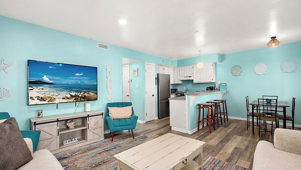 A modern living room with a large TV, teal armchair, and a wooden coffee table.