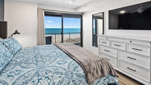 Ein Schlafzimmer mit einem großen Bett, einem Deckenventilator, einem Fernseher, einer Kommode und einem Balkon mit Meerblick.
