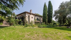 A rustic house with a garden, surrounded by tall trees and a clear sky.