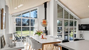 Une cuisine moderne dotée de grandes fenêtres, d’un îlot central et d’un coin repas avec des chaises blanches.