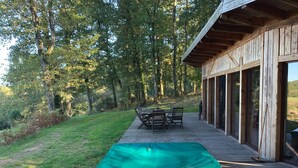 A wooden deck with a green pool table, outdoor furniture, and a glass-enclosed building. - eco-gîte with SPA in the heart of nature, horse riding, Limousin (DOMPIERRE-EGLISES)