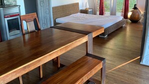 A spacious room with a large wooden dining table, a bed with a wicker headboard, and a view of greenery through large windows. - eco-gîte with SPA in the heart of nature, horse riding, Limousin (DOMPIERRE-EGLISES)