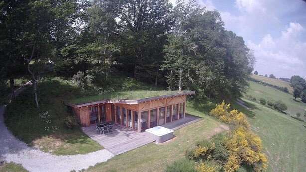 A wooden cabin with a deck and outdoor seating area, surrounded by trees and grass. - eco-gîte with SPA in the heart of nature, horse riding, Limousin (DOMPIERRE-EGLISES)