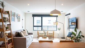 A modern living room with a sofa, chairs, a dining table, and a large window with a view of buildings. - Adanac Revelstoke by Revelstoke Vacations (Revelstoke)