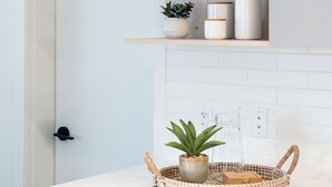 A kitchen with white cabinets, a wooden shelf with wine glasses, a hanging light, and a woven basket with a plant. - Adanac Revelstoke by Revelstoke Vacations (Revelstoke)