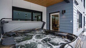 A hot tub with a wooden deck and a house in the background. - Adanac Revelstoke by Revelstoke Vacations (Revelstoke)