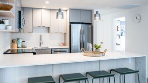 A modern kitchen with a large island, stainless steel appliances, and green bar stools. - Adanac Revelstoke by Revelstoke Vacations (Revelstoke)