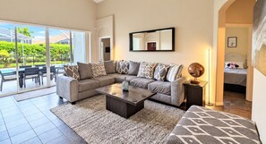 A modern living room with a sectional sofa, a coffee table, and a large window overlooking a patio area.