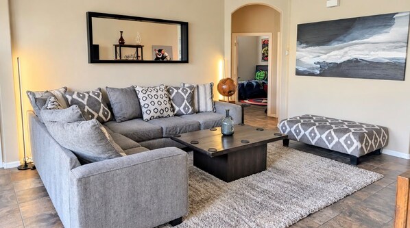 A modern living room with a grey sofa, patterned cushions, a coffee table, and a rug.