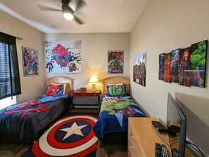 Une chambre avec deux lits, chacun agrémenté de linge de lit sur un thème particulier, un ventilateur de plafond et des œuvres d’art murales, notamment des affiches de super-héros.
