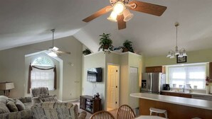 A living room with a sofa set, a dining table with chairs, a kitchen area with appliances, and a ceiling fan. - 14022 Maple Way (Mercersburg)