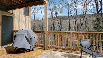 A covered deck with a chair and a covered grill.