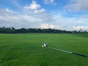 Un terrain de golf sous un ciel dégagé, avec un mât de drapeau bien visible au premier plan.
