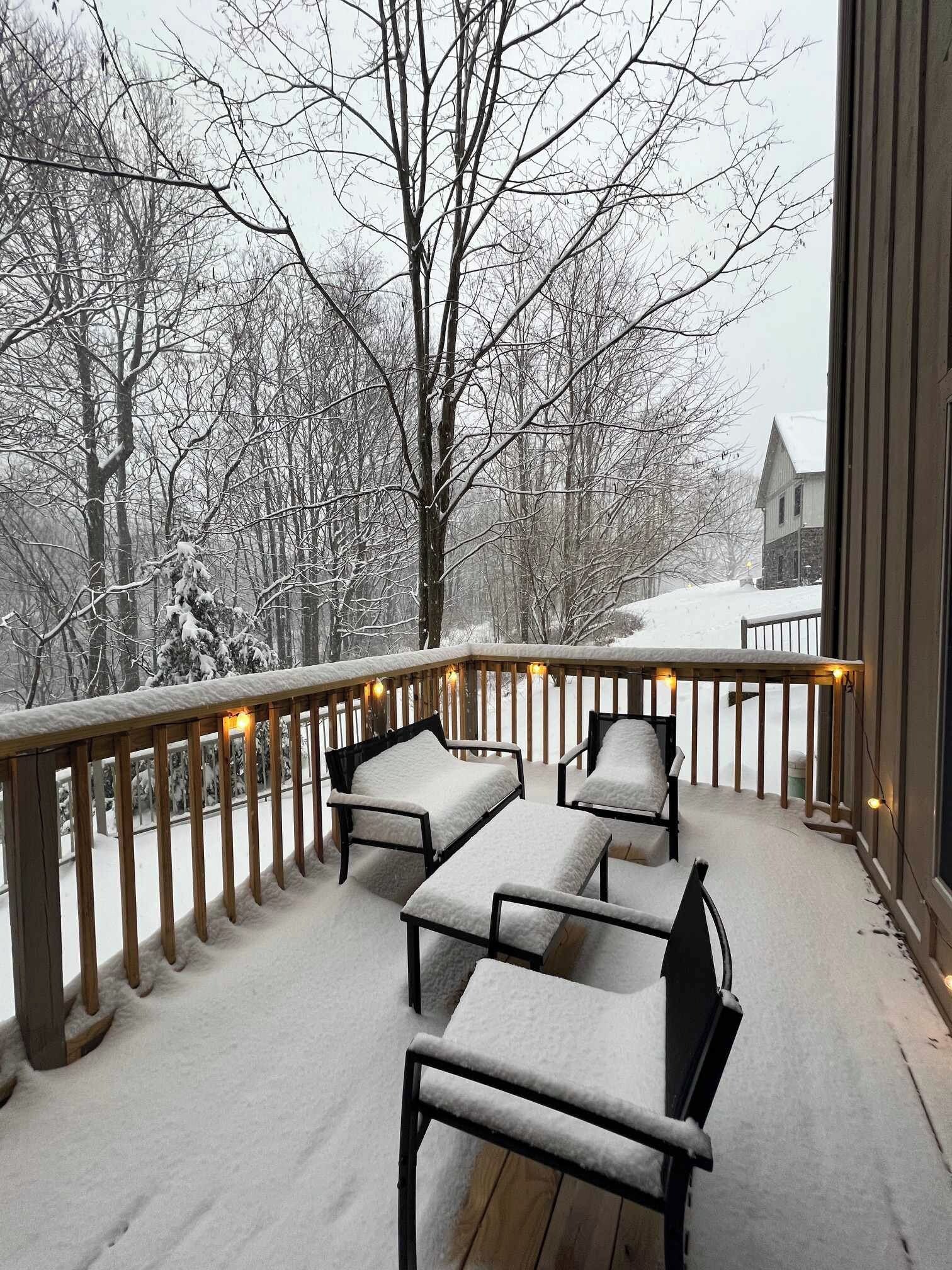 A snow-covered deck with outdoor seating and a view of a snowy landscape.