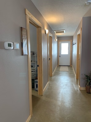 Corredor com portas de madeira, termostato e luminária na parede.