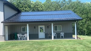 A covered outdoor area with a metal roof, a door, and two windows. There are two white plastic chairs and a small table. - UpNorth Getaway with access to ATV UTV Snowmobile Trail (Birchwood)