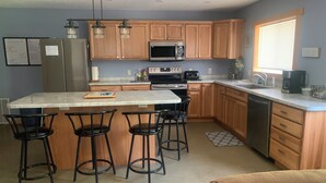 A kitchen with wooden cabinets, a stainless steel refrigerator, a microwave, a stove, and a coffee maker. There are four bar stools around the island. - UpNorth Getaway with access to ATV UTV Snowmobile Trail (Birchwood)