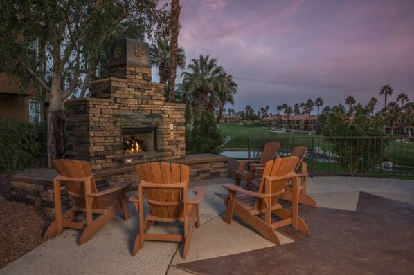 Relax in the outdoor seating area with a fireplace and Adirondack chairs, overlooking the golf course and palm trees.