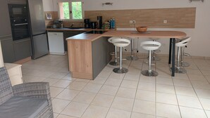 A modern kitchen with a wooden island, bar stools, a refrigerator, and a coffee maker. - Villa de prestige au cœur d’un domaine privé
Piscine privée & sérénité absolue (Le Muy)