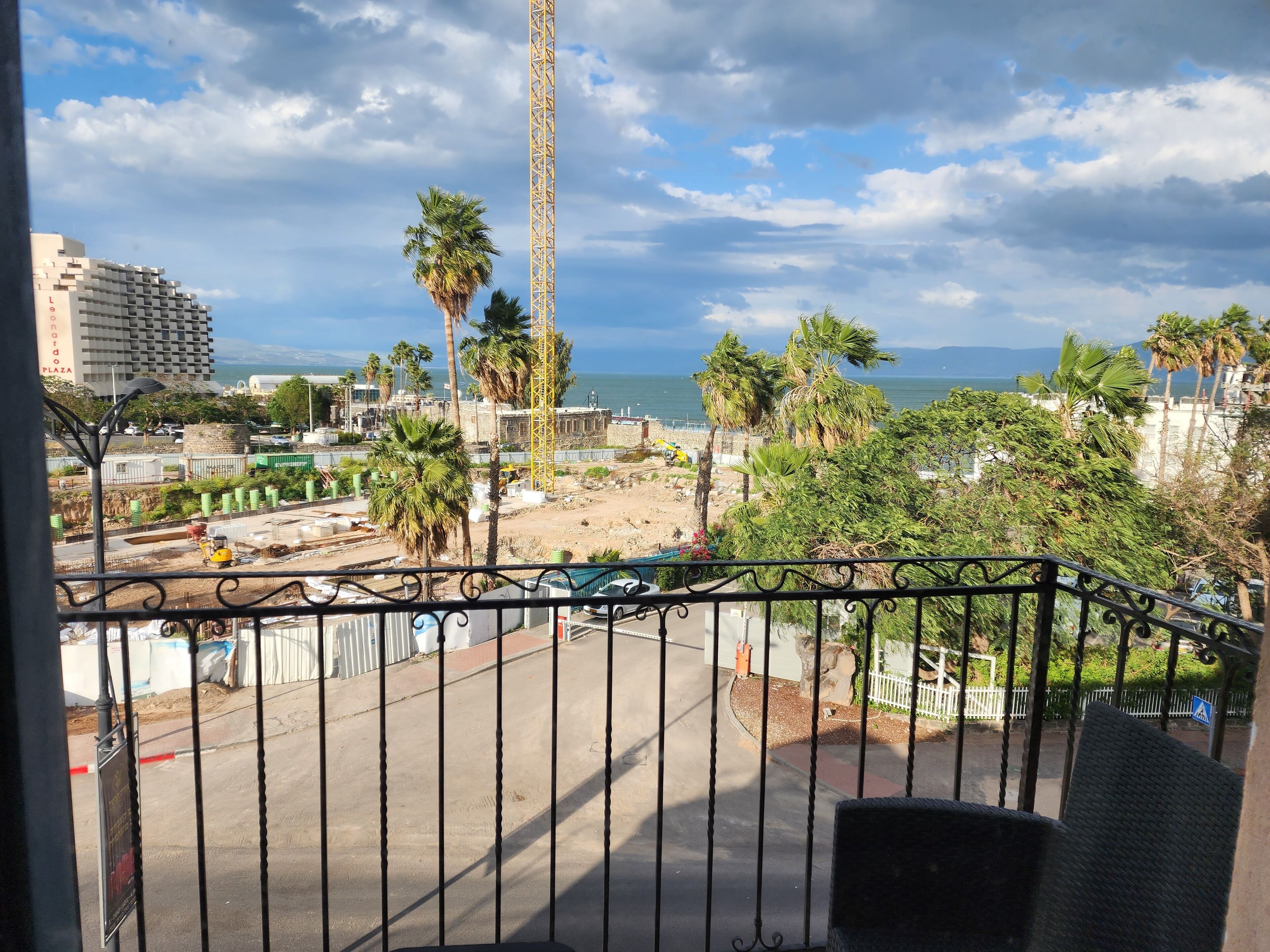 A balcony with a view of a construction site, palm trees, and a building in the background.