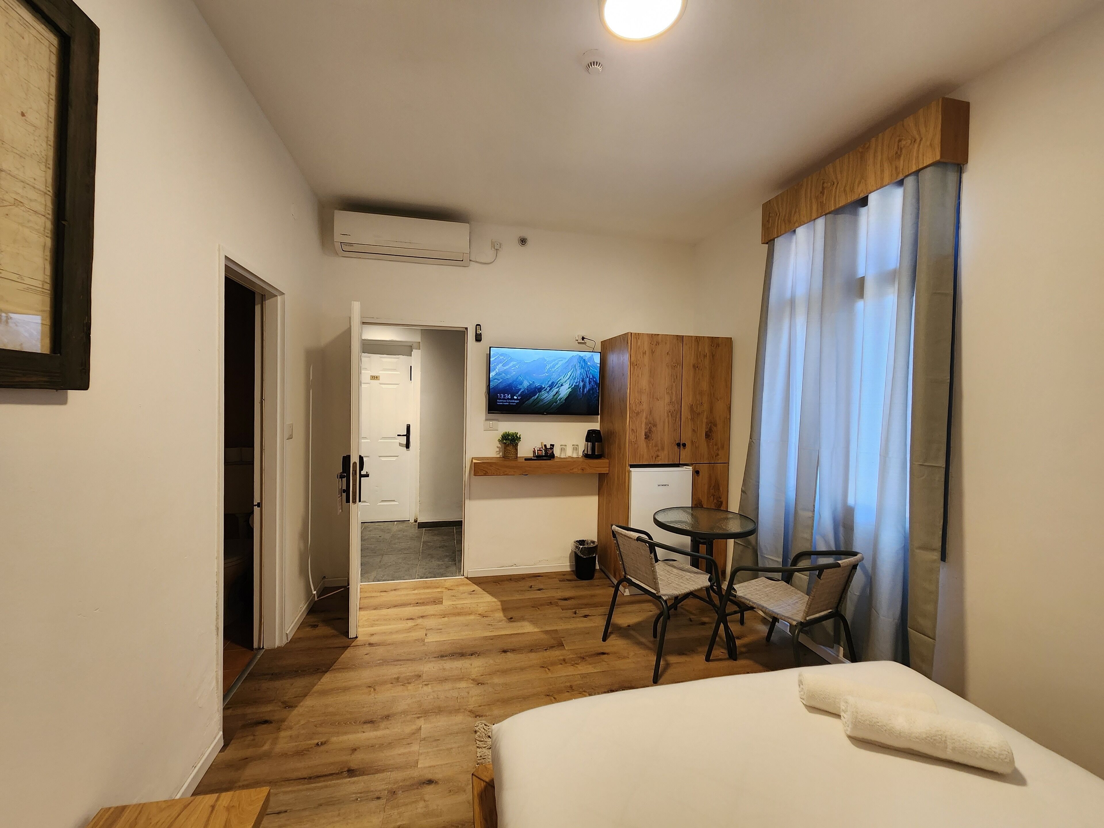 A hotel room with a bed, a desk with a chair, a television, and a small kitchenette.