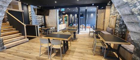 A modern interior with wooden flooring, tables, and chairs arranged for dining.