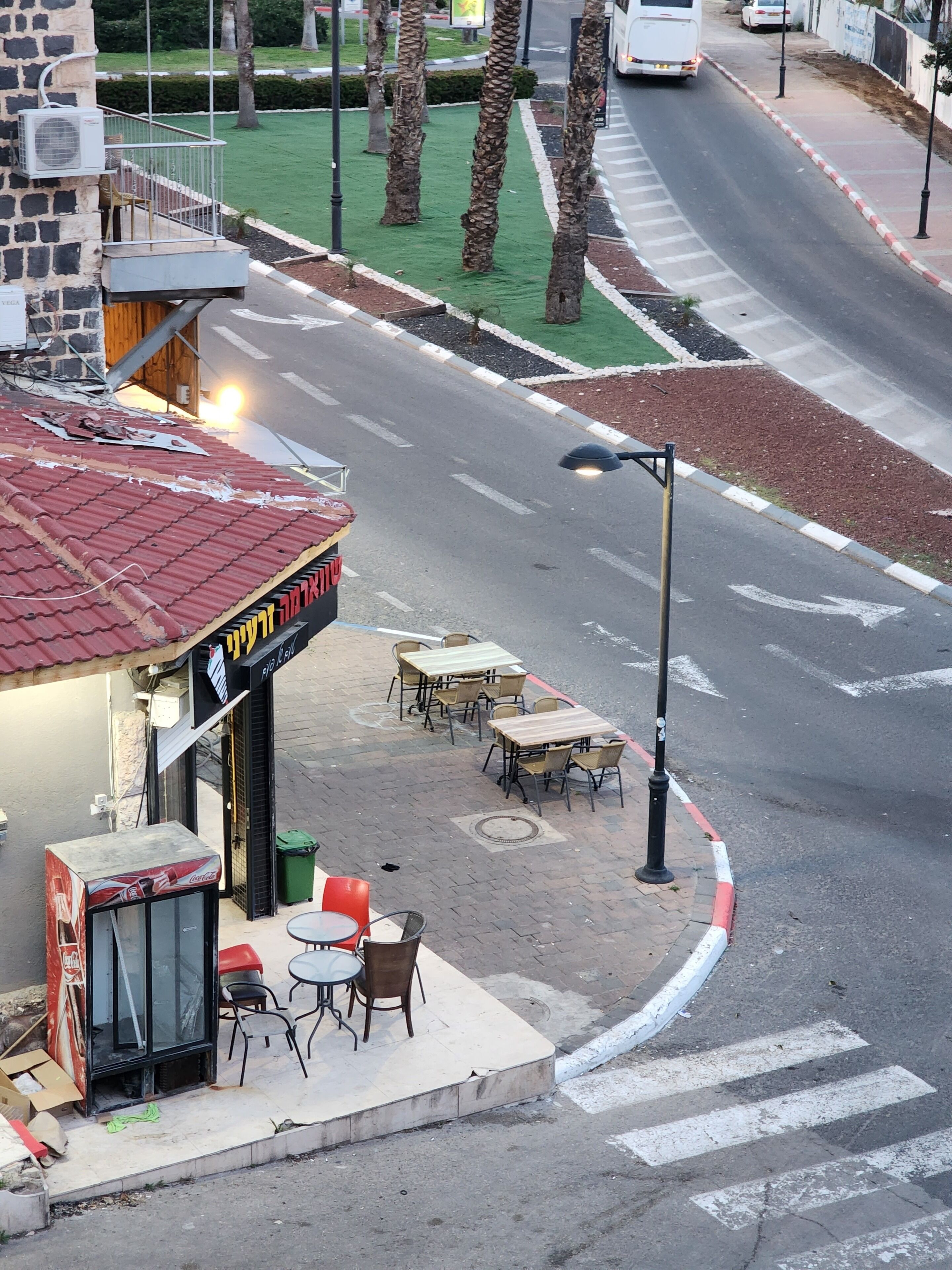 Vista de una calle con un café en la esquina, mesas al aire libre y un paso de peatones.