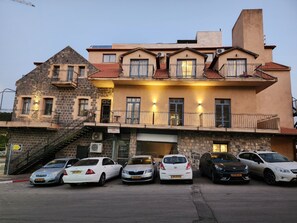 A multi-story building with a stone facade, balconies, and a parking area with several cars. - Tiberia hotel (Tiberias)