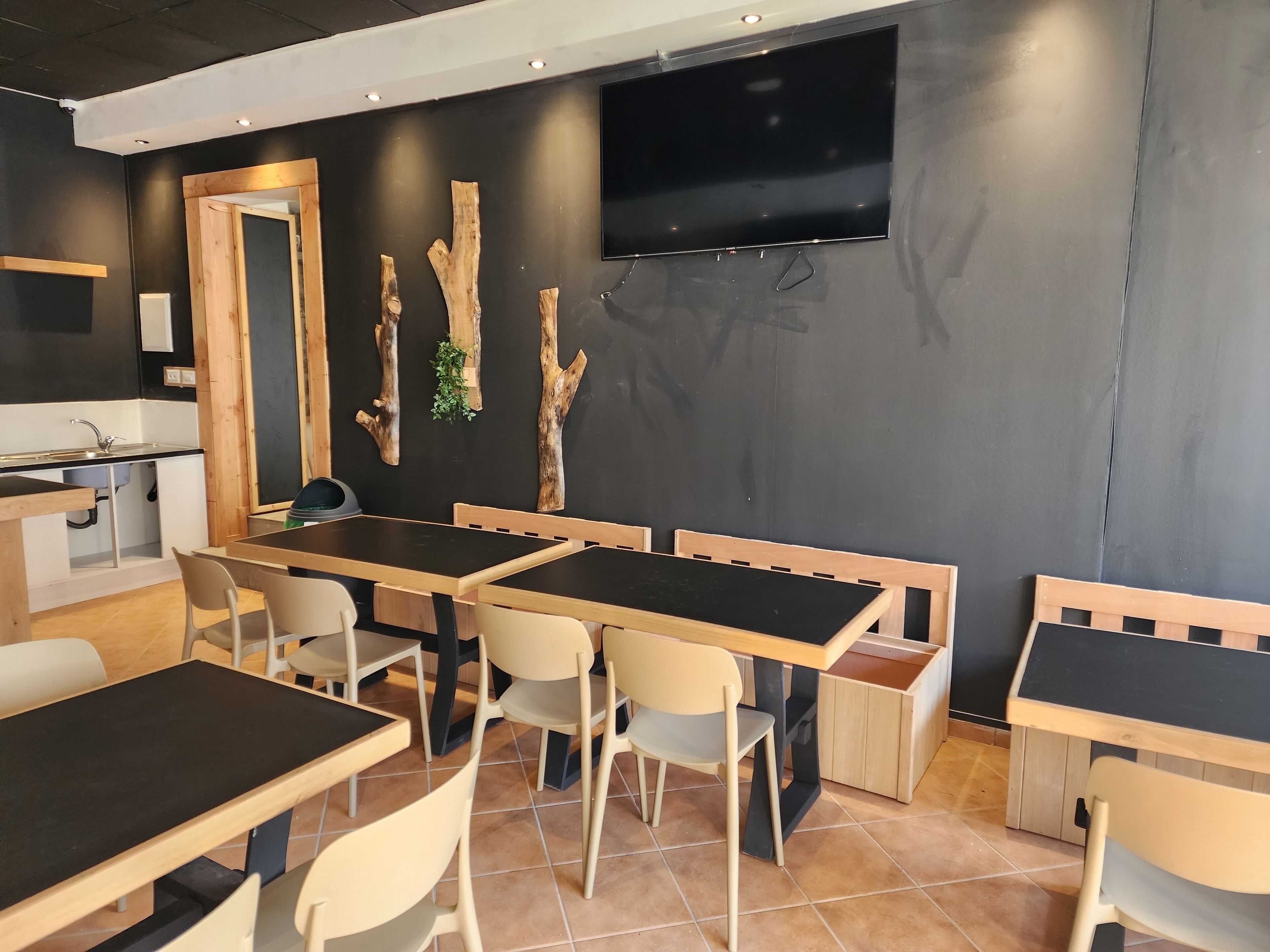 A modern dining area with wooden tables and chairs, a blackboard wall, and a mounted television.