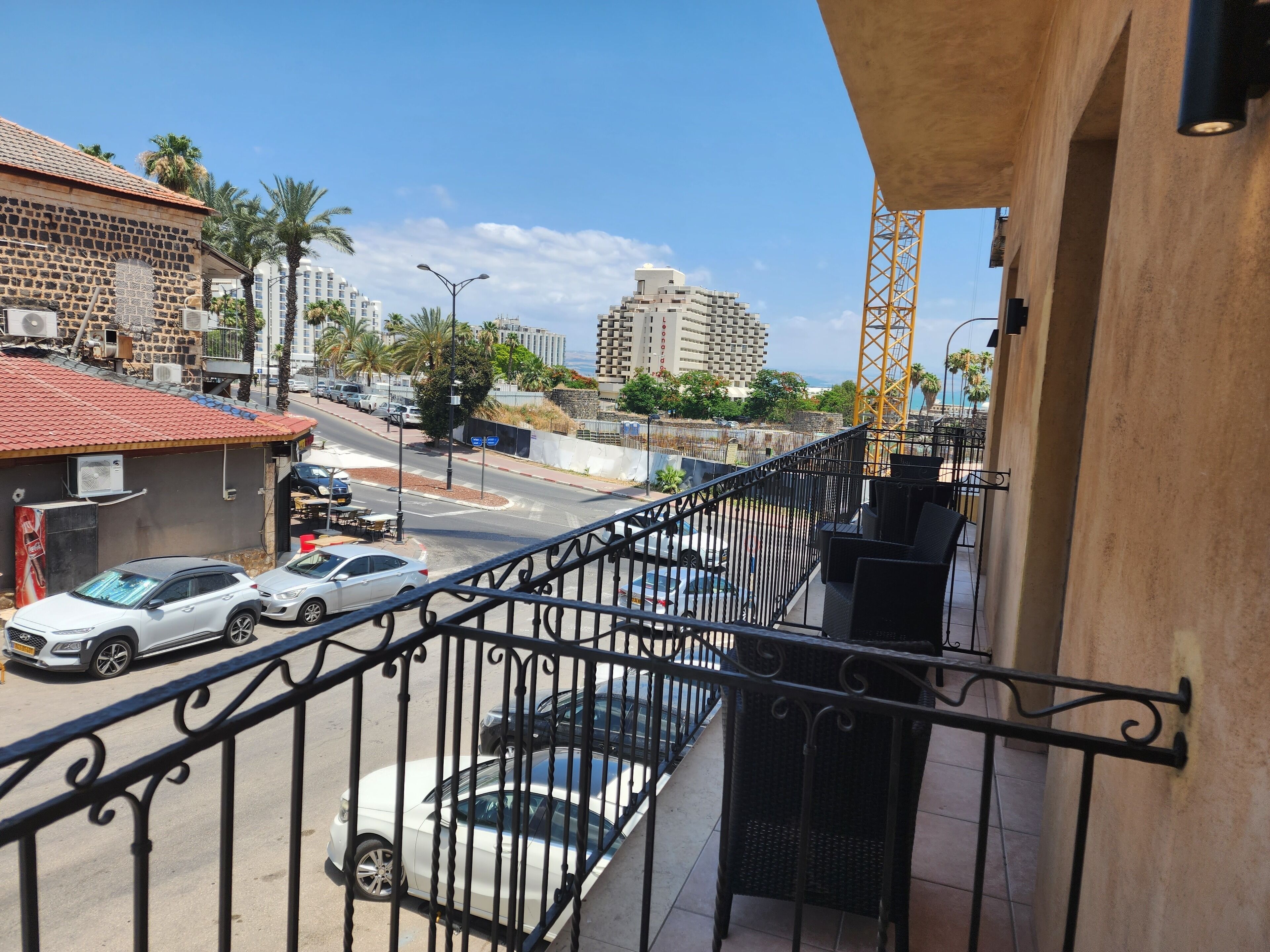 Un balcón con vista a una calle, coches estacionados a lo largo de la vía y edificios al fondo.