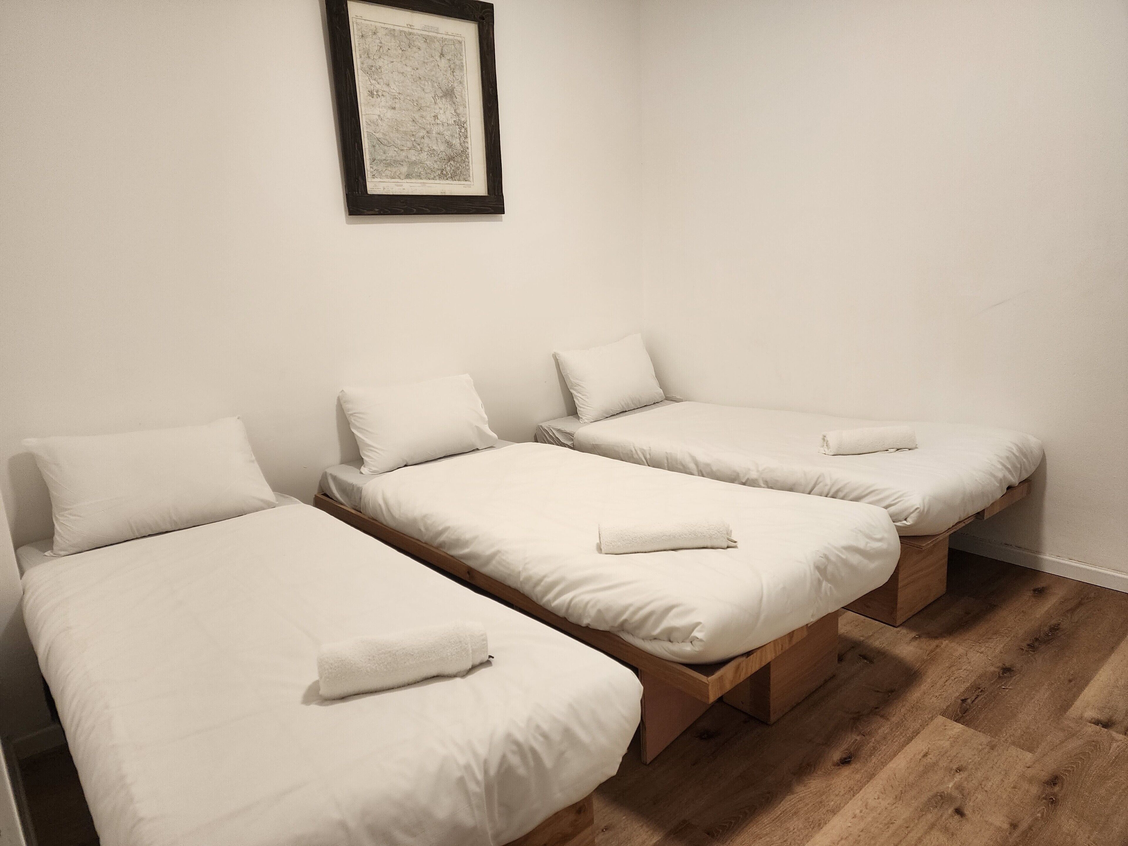 A room with three single beds, each with a pillow and a rolled towel.