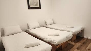 A room with three single beds, each with a pillow and a rolled towel.