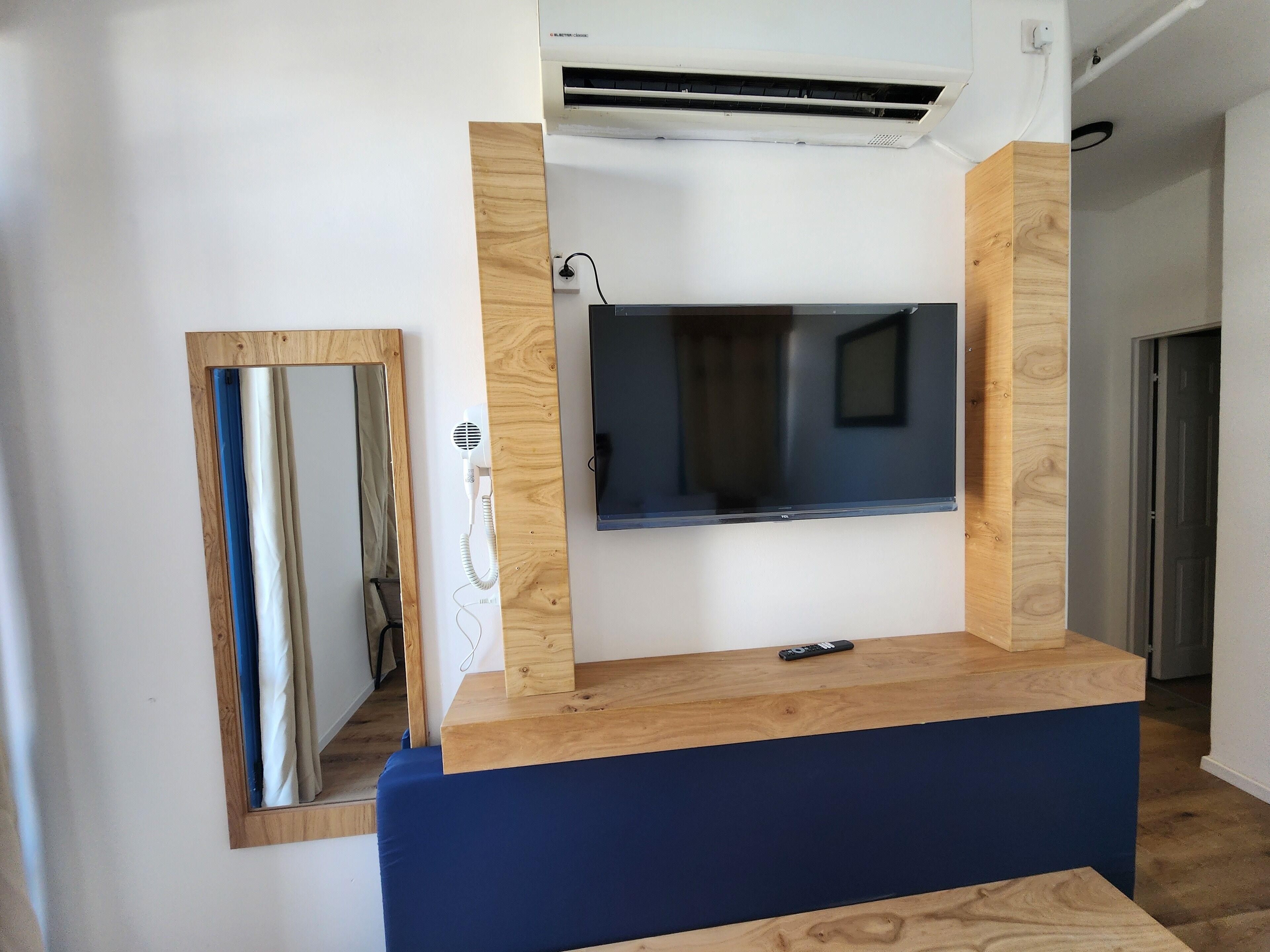 Una habitación con tocador de madera, un espejo y televisor montado.