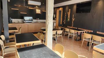 Un restaurant au décor moderne, avec un mélange de tables et de chaises en bois et en noir, une cuisine ouverte et un téléviseur à écran plat fixé au mur.