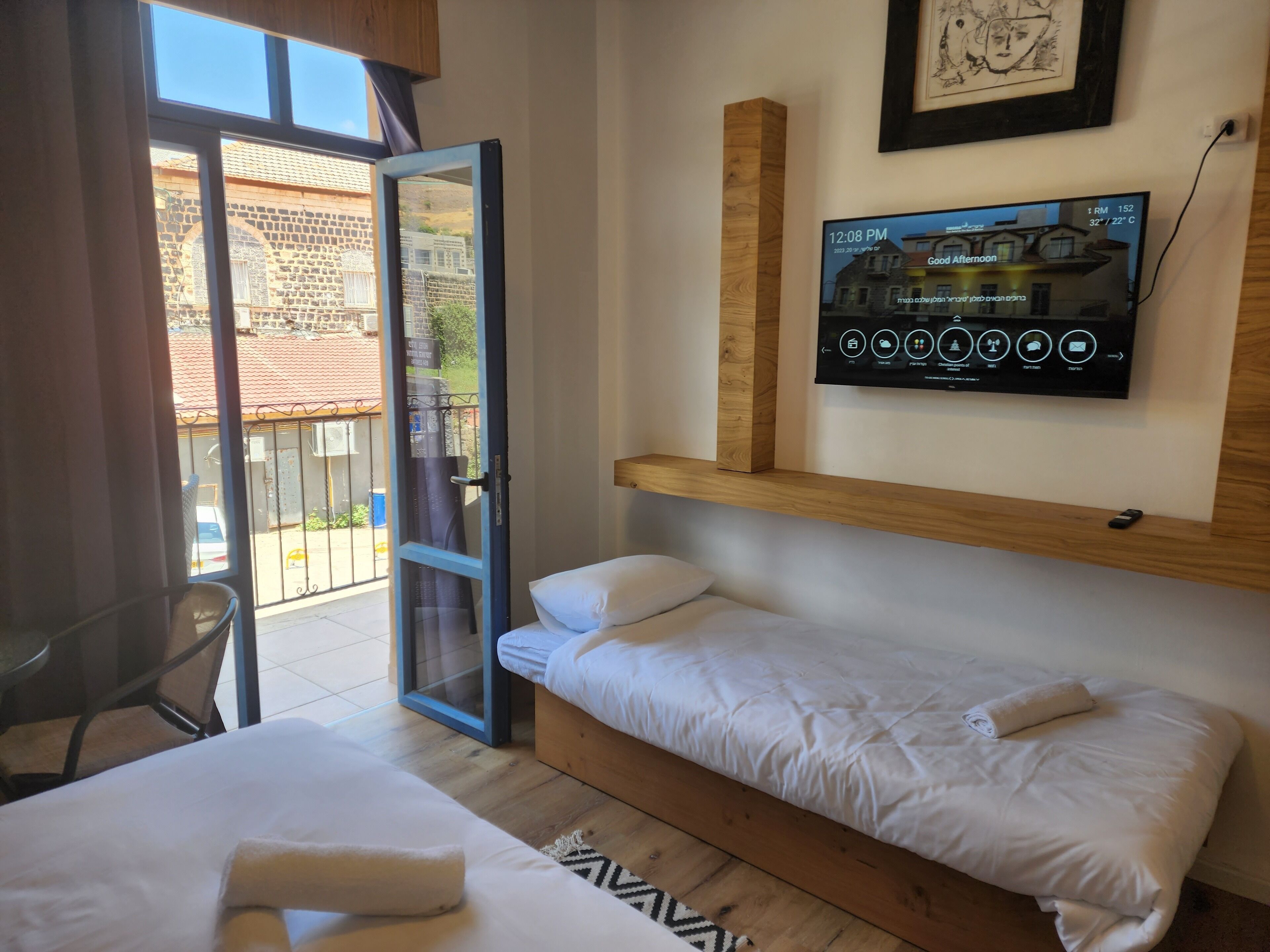 Habitación de hotel con cama, televisión montada en la pared y balcón con vistas al exterior.