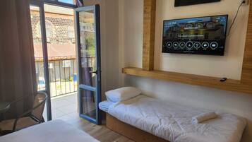 Habitación de hotel con cama, televisión montada en la pared y balcón con vistas al exterior.