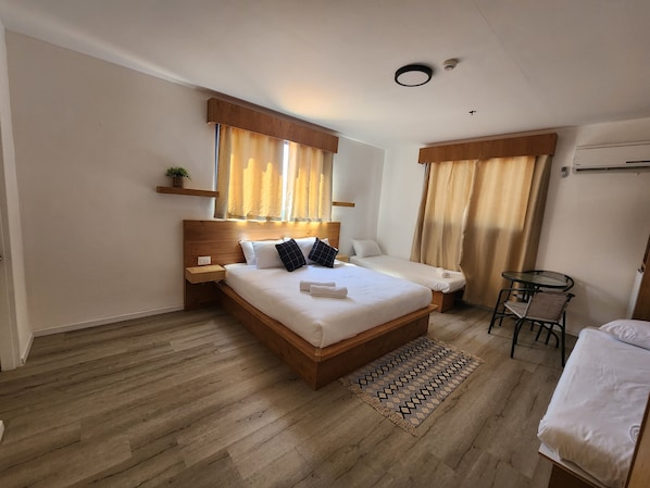 A bedroom with a large bed, a smaller bed, a bedside table, a chair, a small table, and a window with curtains. - Tiberia hotel (Tiberias)