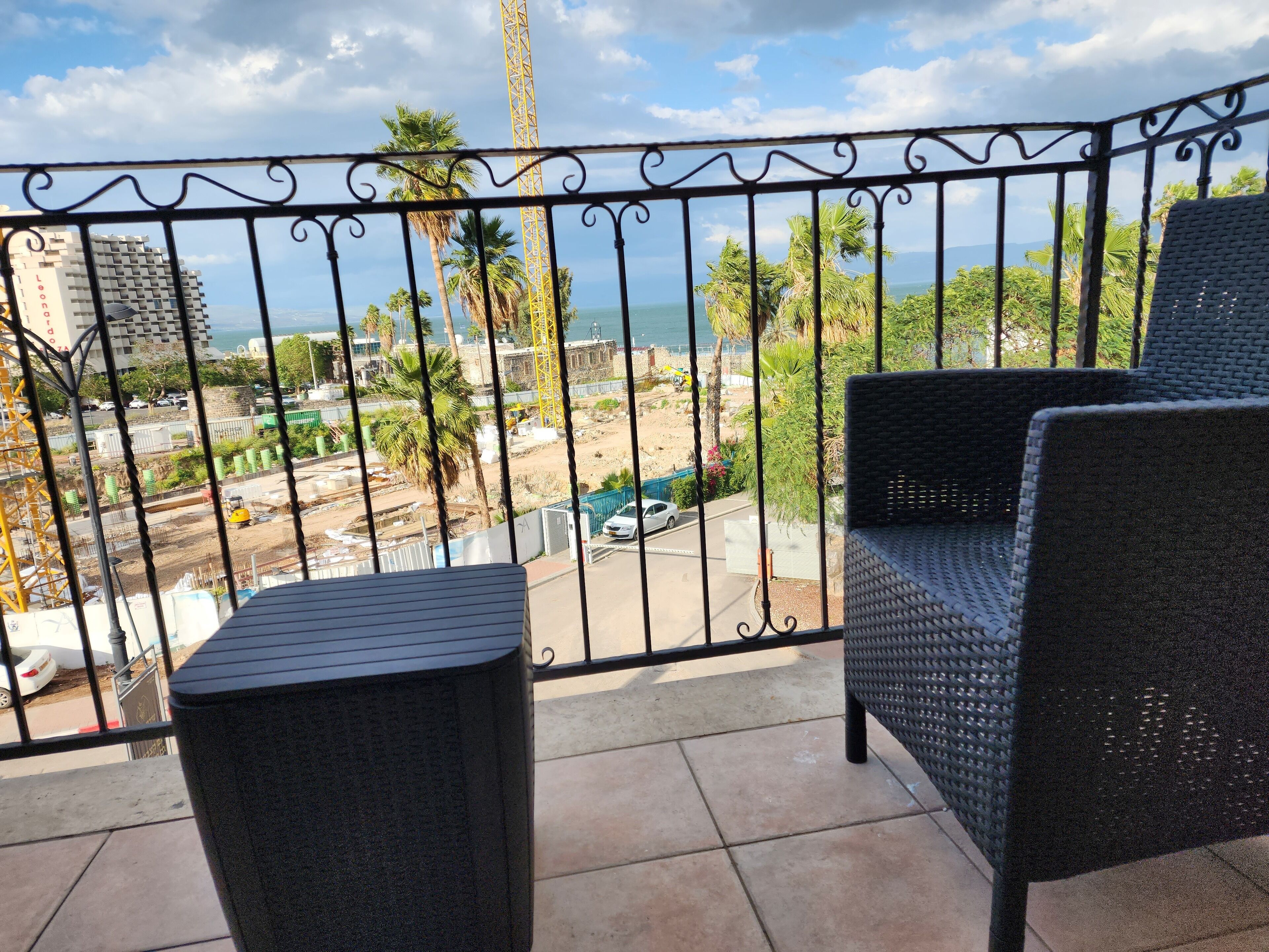 Un balcon doté de meubles en osier, donnant sur un chantier de construction et offrant une vue sur la mer.