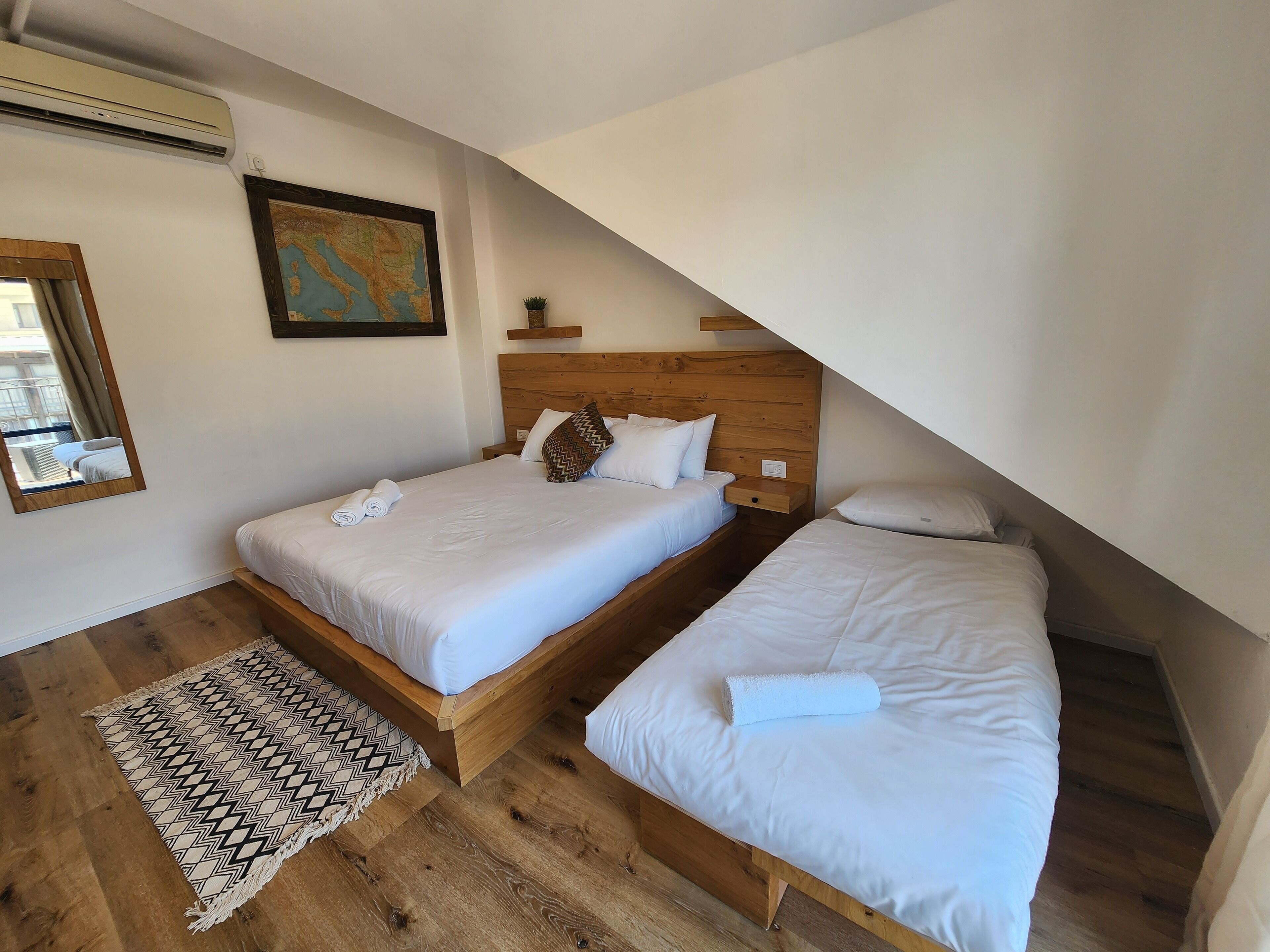 Ein Schlafzimmer mit zwei Betten, einem hölzernen Kopfteil, einer Karte an der Wand und einem Spiegel.