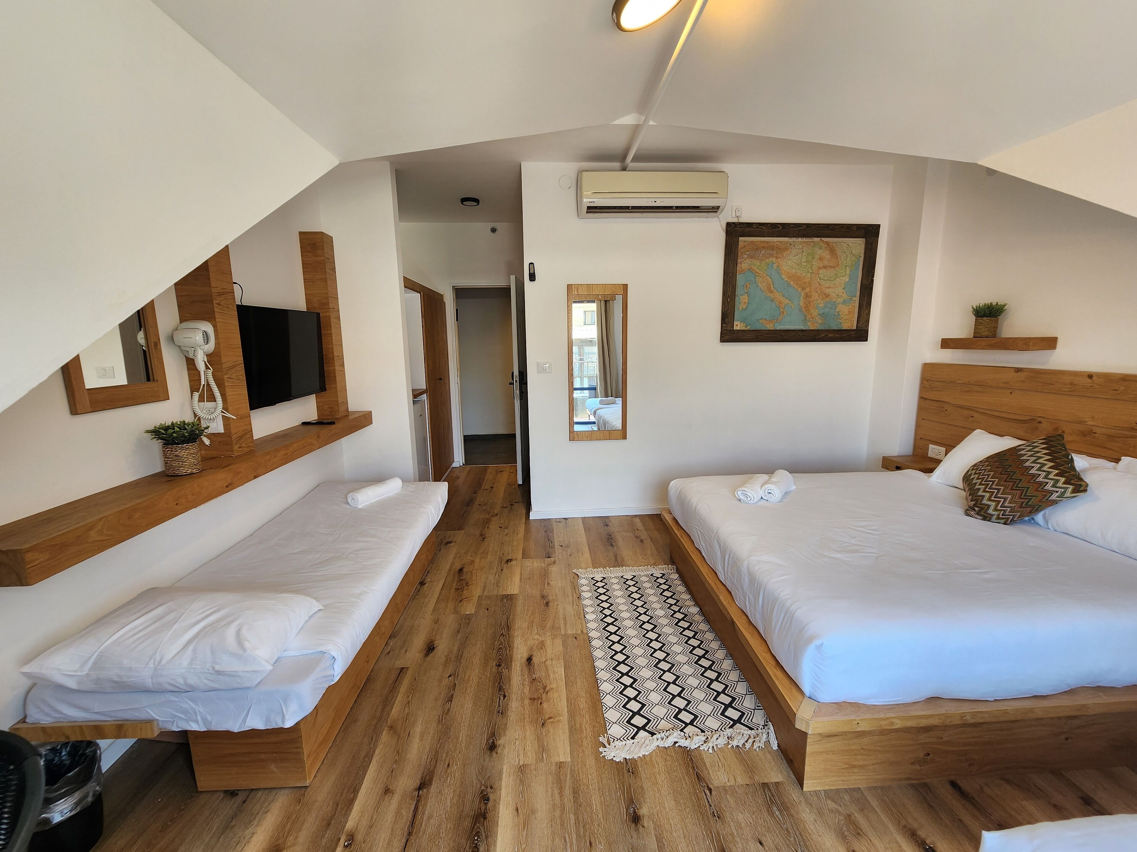 Habitación de hotel con dos camas, piso de madera, un mapa en la pared y un equipo de aire acondicionado.