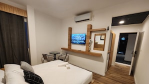 A hotel room with a bed, a small table with chairs, a TV mounted on the wall, and an air conditioning unit. - Tiberia hotel (Tiberias)