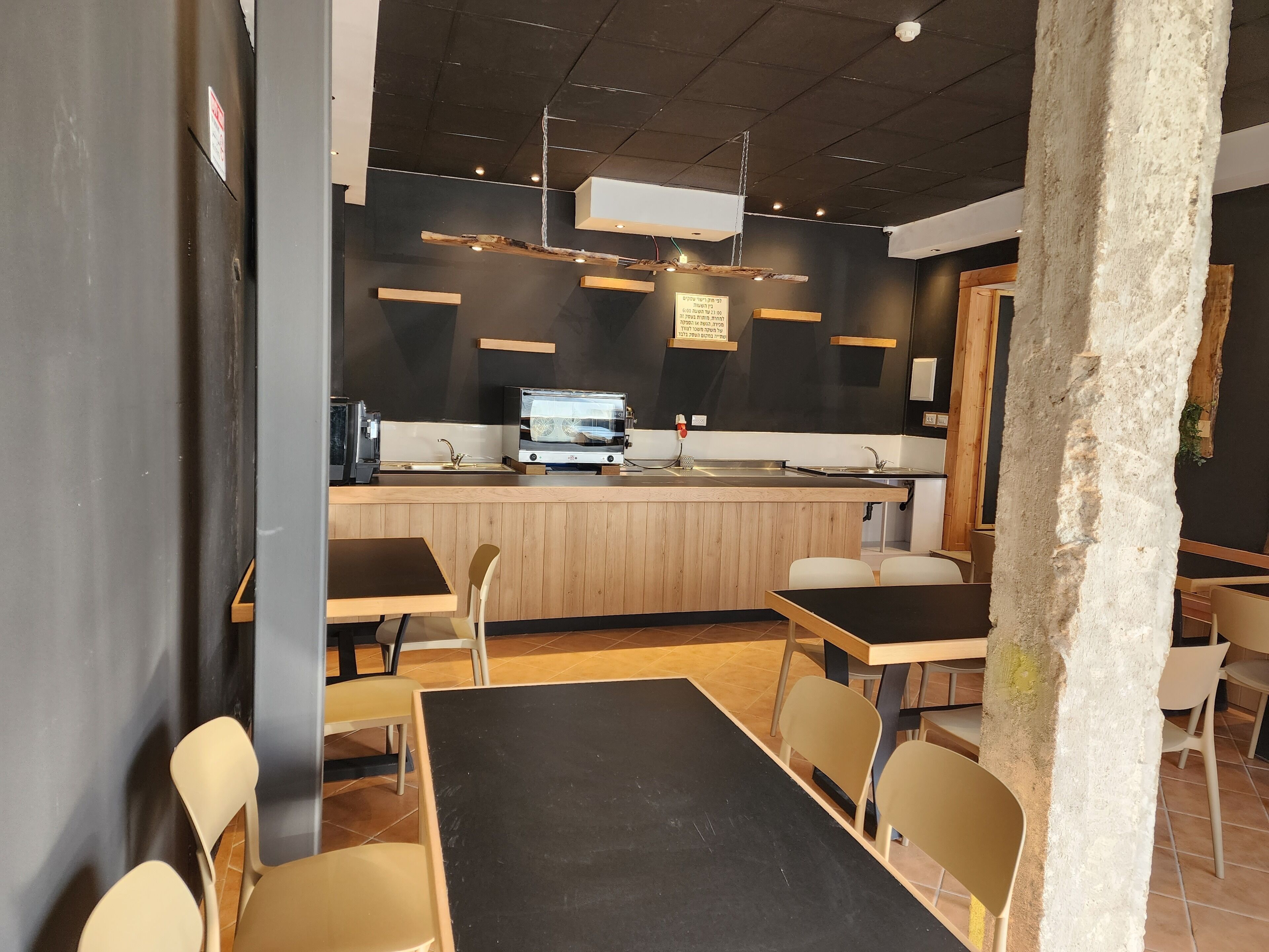 Un interno ristorante moderno con un bancone centrale a isola, sedie in legno e un tavolo nero.