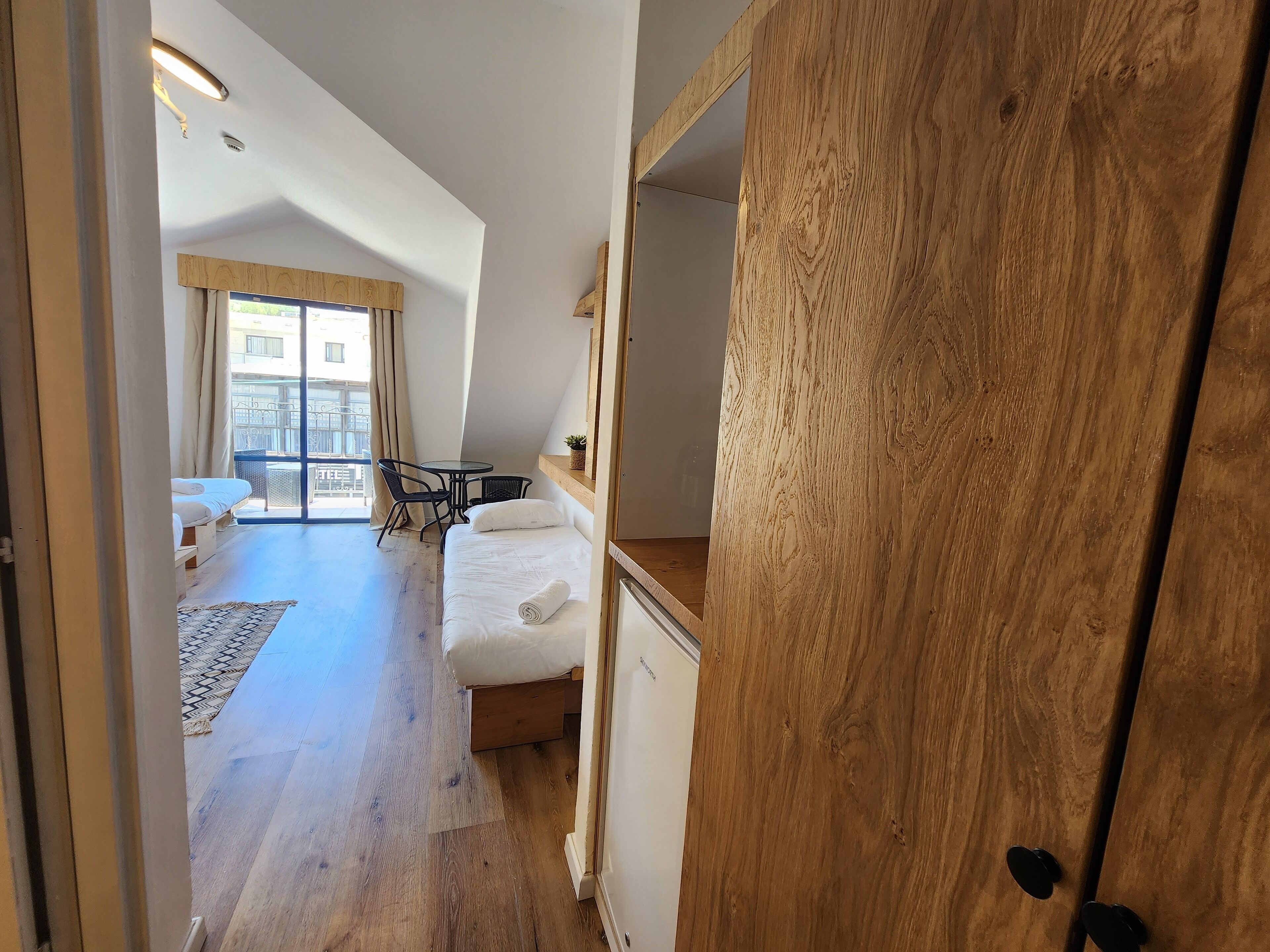 Un dormitorio con cama, una mesita y una silla. Tiene un balcón con vista a la ciudad.