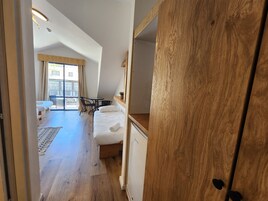 Un dormitorio con cama, una mesita y una silla. Tiene un balcón con vista a la ciudad.