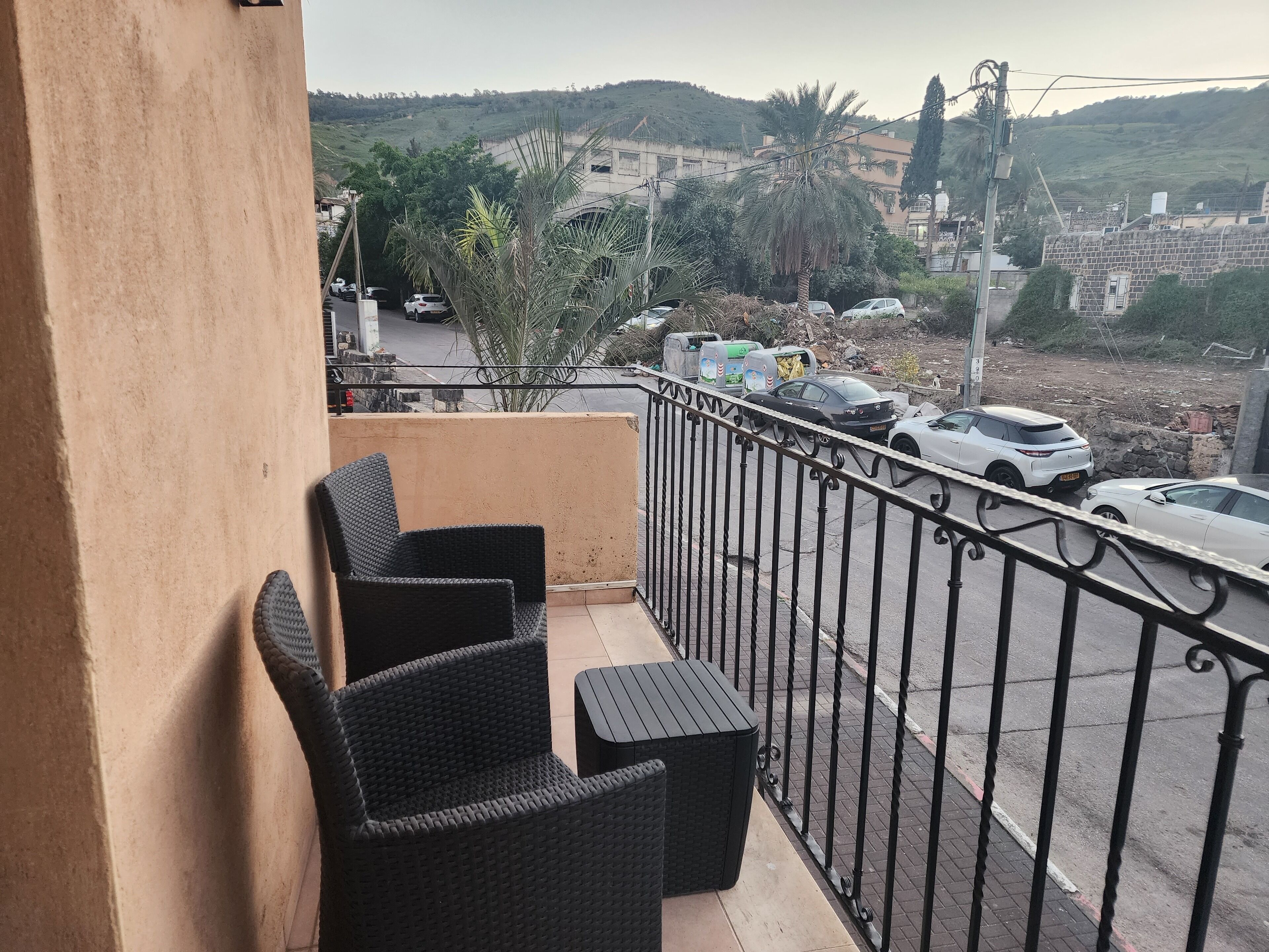 Ein Balkon mit Korbmöbeln, Blick auf geparkte Autos und eine hügelige Landschaft im Hintergrund.