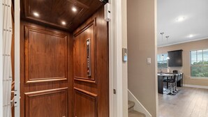 A wooden elevator with a control panel, leading to a kitchen area with a window and a staircase. - Your Home Away From Home in the Texas Hill Country, Georgetown TX (Georgetown)