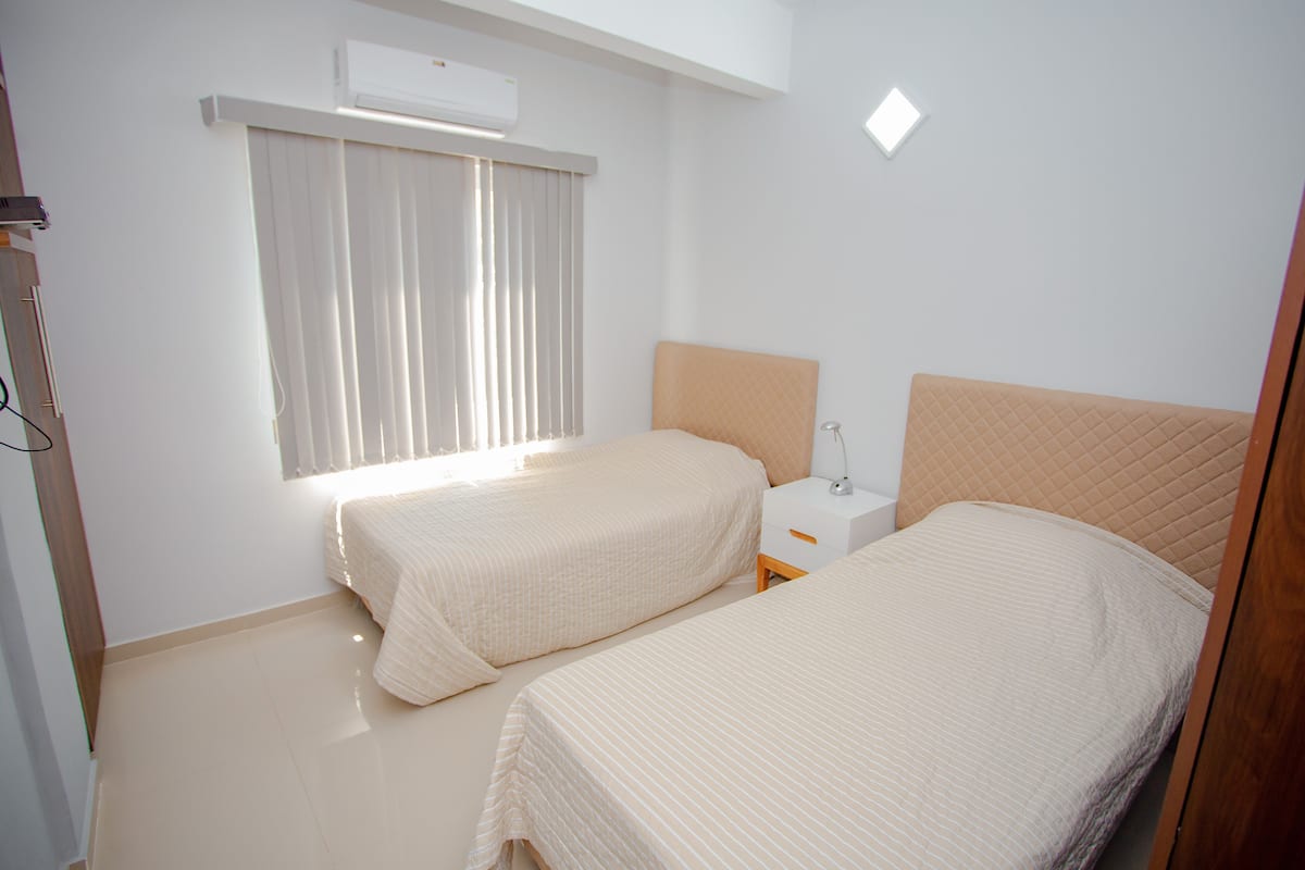 A bedroom with two beds, a nightstand, a lamp, and an air conditioning unit.