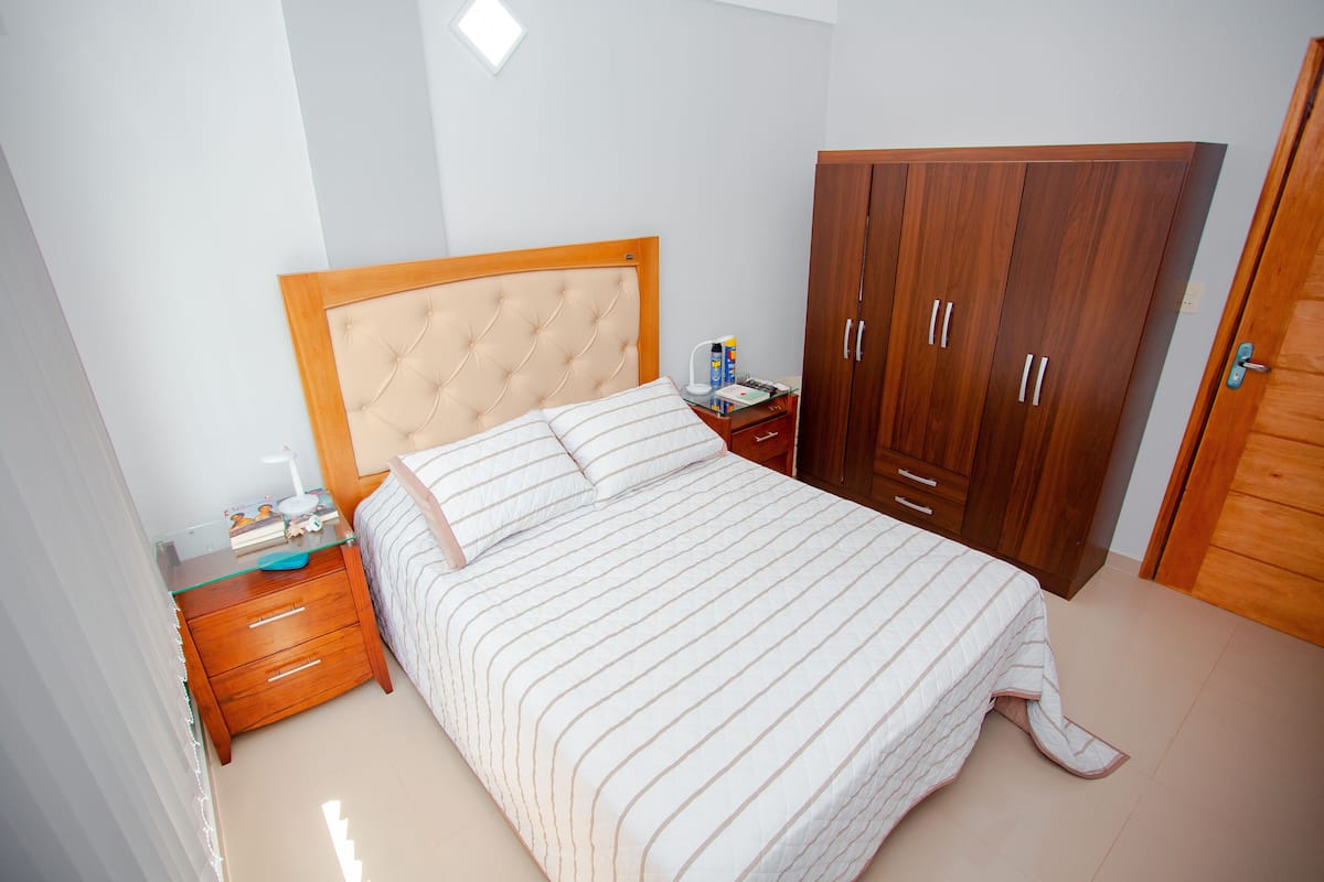 A bedroom with a bed, wooden wardrobe, bedside table, and a nightstand.