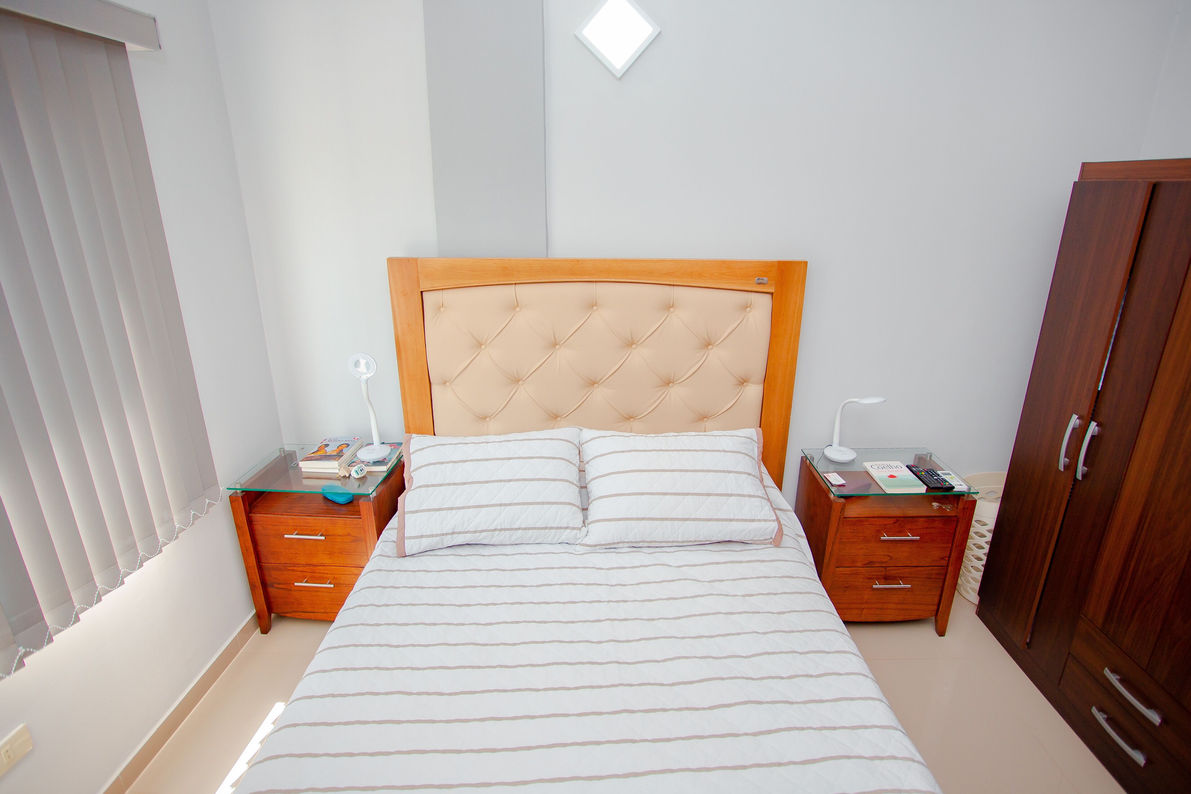 Un dormitorio ordenado con cama, mesitas de noche, armario y ventana con persianas.