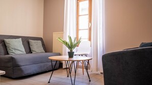 Een woonkamer met een grijze bank, een klein rond tafeltje met een potplant en een witte stoel.